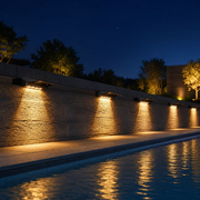 Solar deck lights along a pool deck wall at night